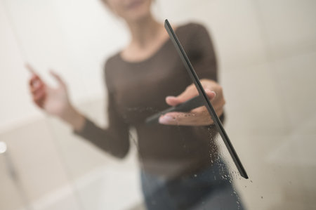 Dark-haired woman cleaning the shower cabin and looking contented
