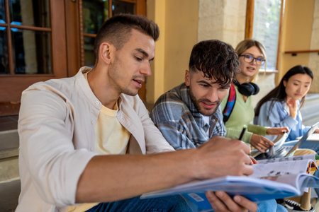 Students studying together while sitting on stairs in university campusの写真素材
