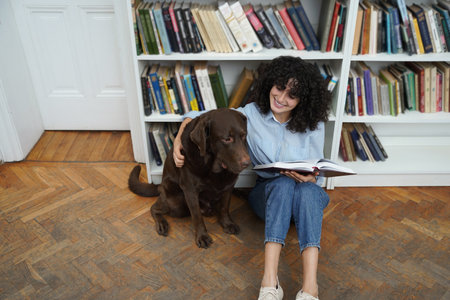 Curly-haired woman sitting on the floor in a library with a dogの写真素材