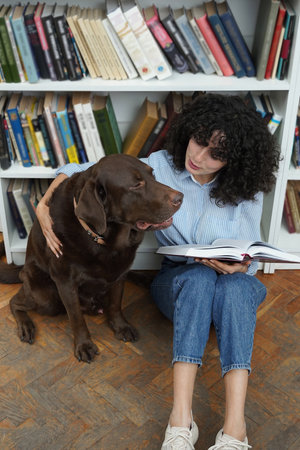 Woman and a dog sitting on the floor in a library, woman reading a book