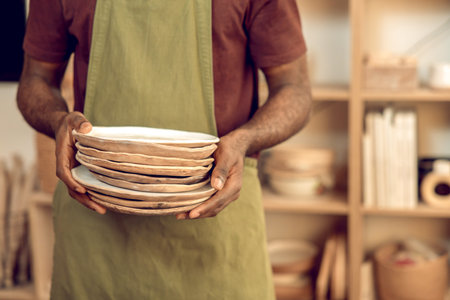 Man in apron standing with ceramic plates in handsの写真素材