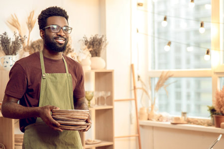 Dark-skinned man in eyeglasses working with pottery in his workshop