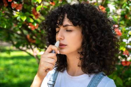 Dark-haired young woman using nasal spray while having allergy symptoms