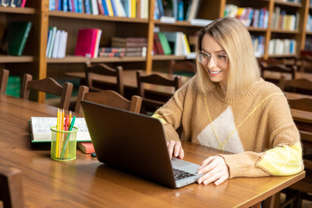 Young blonde woman working on a laptop in the library