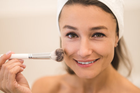Waist up of a woman doing make up and applying powder on her face