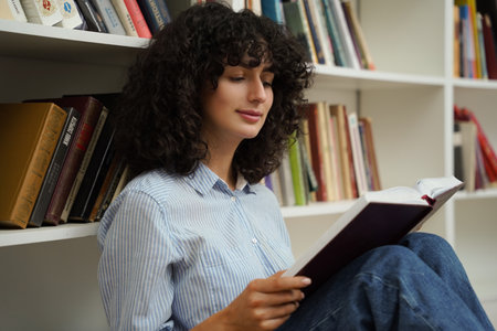 Student woman reading book while sitting on floor in library