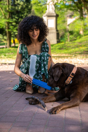 Curly-haired young woman giving some water to a thirsty dog