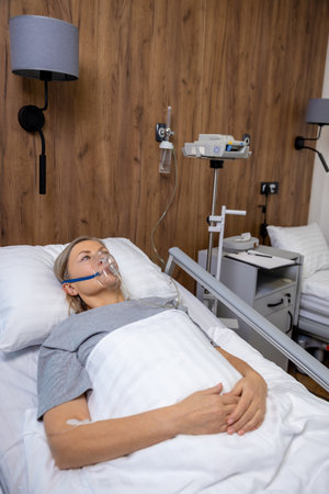 Blonde mid aged woman lying in bed in hospital with an oxygen mask on her face
