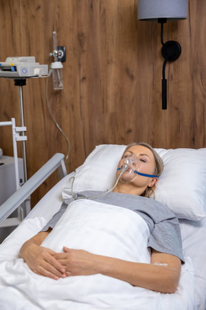 Blonde mid aged woman lying in bed in hospital with an oxygen mask on her face