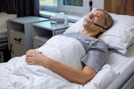 Blonde mid aged woman lying in bed in hospital with an oxygen mask on her face