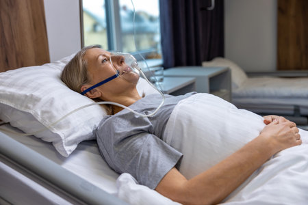 Blonde mid aged woman lying in bed in hospital with an oxygen mask on her faceの写真素材