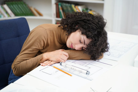 Exhausted woman architect working with blueprints in library and falling asleepの写真素材