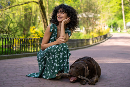 Cute curly-haired young woman looking dreamy having a walk with a dog in the parkの写真素材