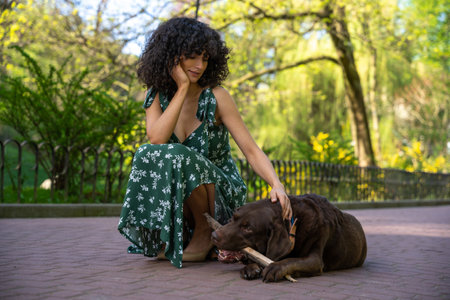 Cute curly-haired young woman looking dreamy having a walk with a dog in the park