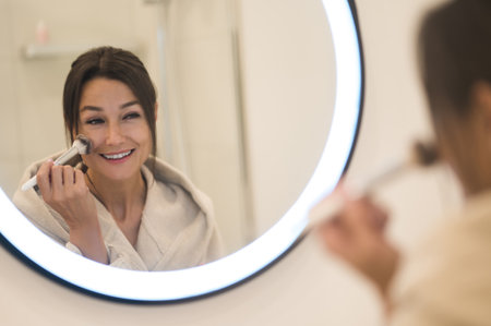 Cute caucasian dark-haired woman at the mirror in the bathroomの写真素材