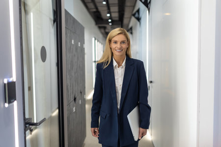 Confident businesswoman holding laptop while standing in modern office hallの写真素材