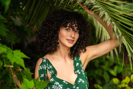 Cheerful woman with dark curls among tropical leavesの写真素材