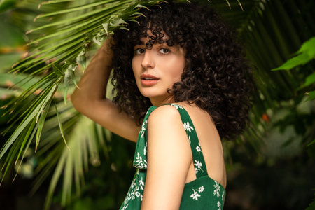 Joyful woman with dark curly hair surrounded by green leavesの写真素材