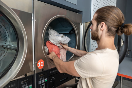 Busy man doing household chores loading washing machine at public laundry