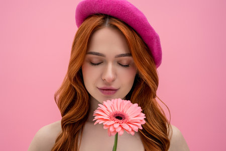 Pretty and sweet young woman in pink beret with a flower in hands looking dreamyの写真素材