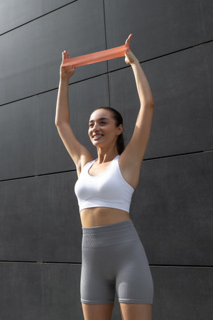Young fit woman doing stretching for arms with fitness band