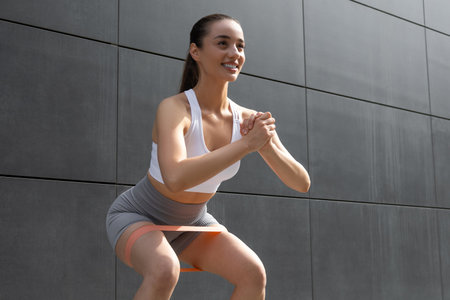 Caucasian young woman doing squats with fitness band