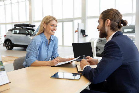 Woman buying new automobile completes purchase with male seller in car showroomの写真素材