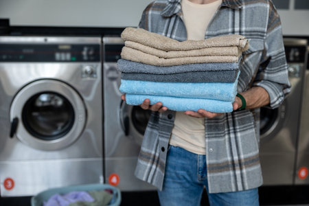 Unrecognizable male with folded towels at industrial laundromat