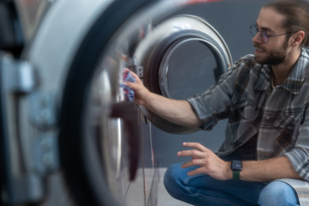 Hard working bearded man washing clothes at self-service laundromat
