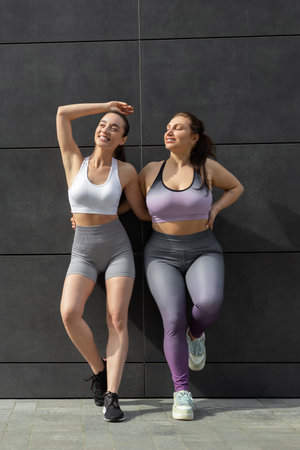Two you women in sportswear standing near the wall and looking confident