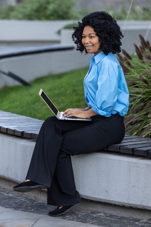 Brunette woman with laptop sitting on a bench and workingの写真素材