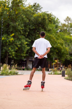 Tall dark-haired young man on rollers in the park having a ride