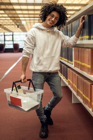 Man student in library reaching for book from shelf preparing for university seminarsの写真素材