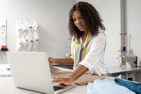 Woman owner of small workshop using laptop to design and make custom garments in her studio