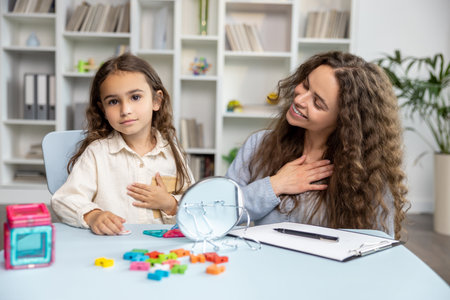 Good-looking young speech therapist working with a cute girl on her articulation