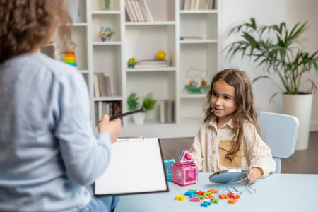 Cute little girl sitting at the table and having a training session with speech therapistの写真素材