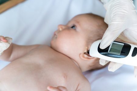 Doctor using infrared ear thermometer to check baby boys temperature during medical examination