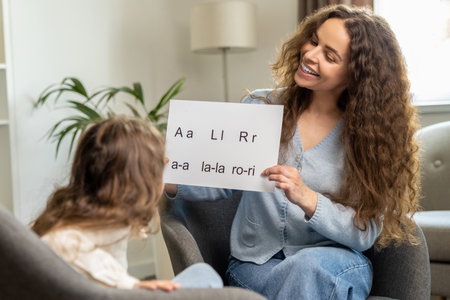 Cute smiling young speech therapist with table with written syllables in handsの写真素材