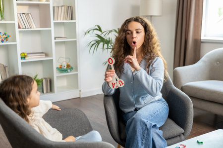 Long-haired female speech therapist showing exercises to a little girlの写真素材