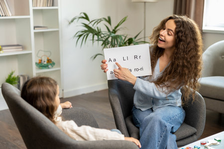 Curly-haired speech therapist demonstrating tables with syllabled to a kidの写真素材