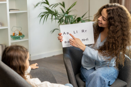Curly-haired speech therapist demonstrating tables with syllabled to a kidの写真素材
