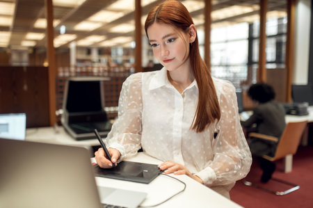 Ginger pretty young woman sitting at the table and looking busyの写真素材