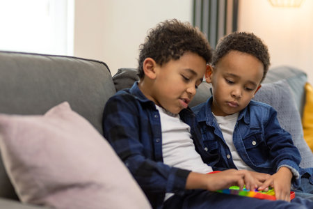 Boys playing with rainbow popit using relieving toy while sitting on the sofa togetherの写真素材