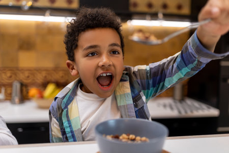 Dark-skinned boy sitting at the table and eating cerealsの写真素材