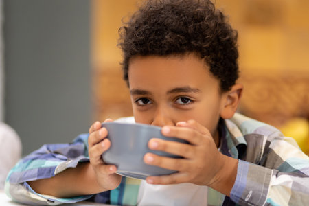 Curly-haired boy sitting in the kitchen and drinking milkの写真素材