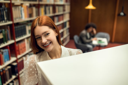 Ginger cute girl working in the library with her friendの写真素材