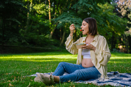 Pretty pregnant young woman eating lunch in the park