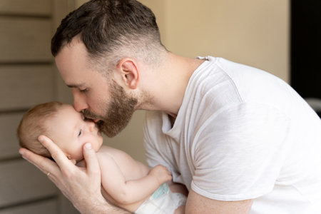 Bearded man young father kissing newborn baby girl or boy in home interior