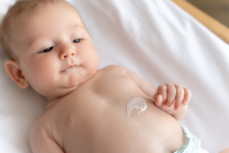 Infant child with lotion on his belly lying on white sheetの写真素材