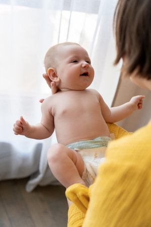 Young mom in bedroom or nursery room interior holding cute newborn little child